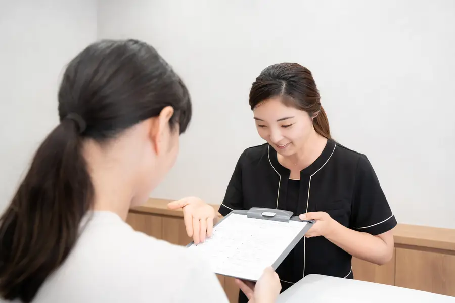 受付で問診票の記入方法を説明するスタッフ